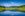 Panoramic view of idyllic summer landscape in the Alps with clear mountain lake and fresh green mountain pastures in the background