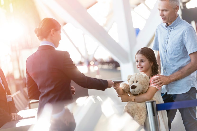Flight attendant checking ticket of girl with teddy bear in airport