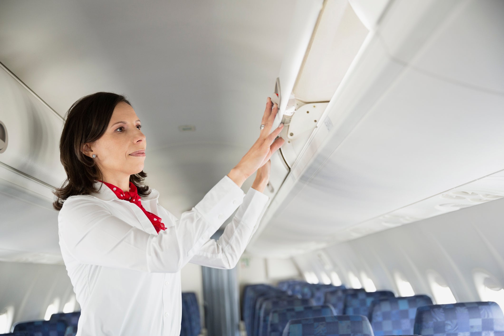 Flight attendant closing overhead bin in airplane