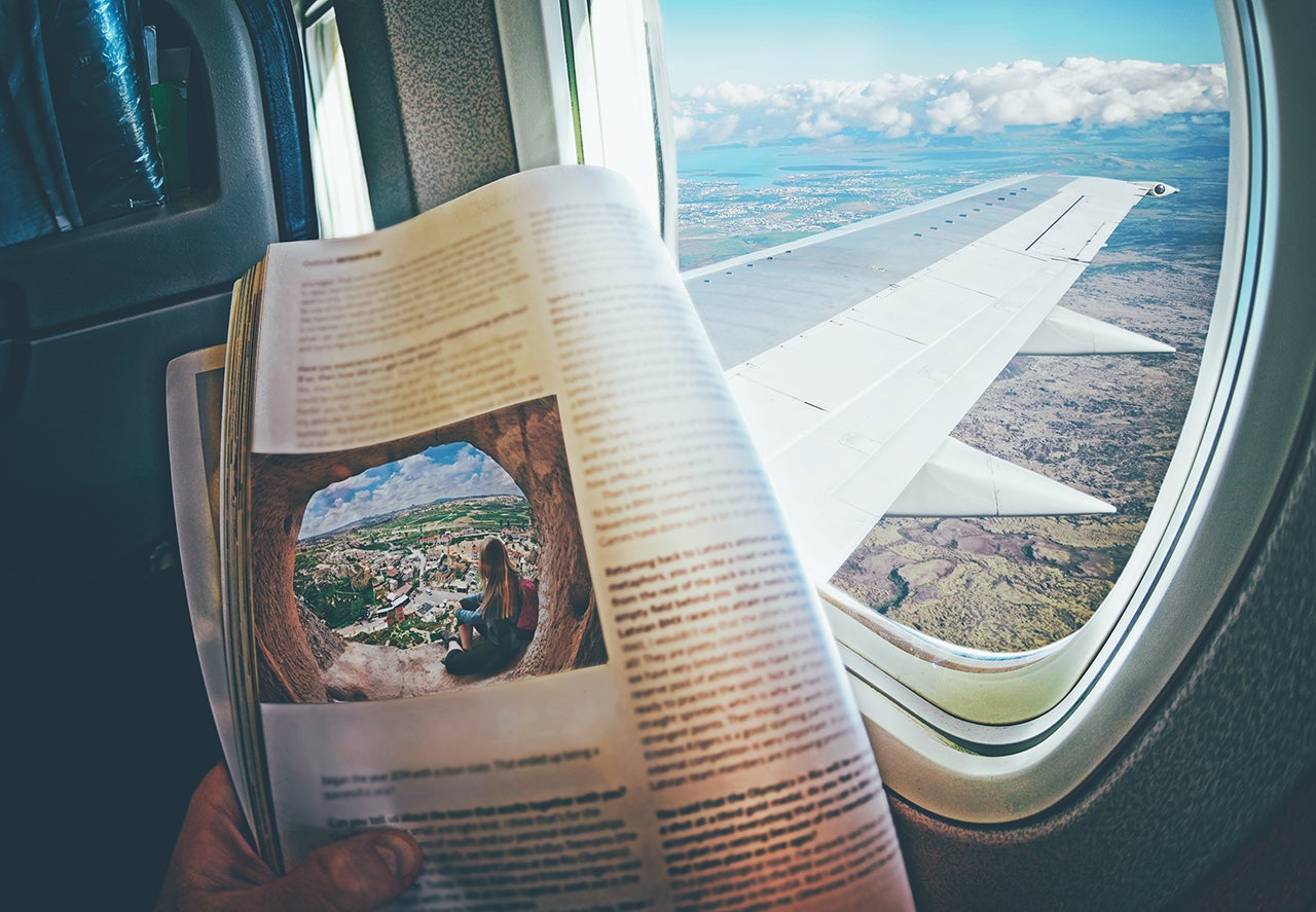 Woman is sitting  by window on a plane with magazine