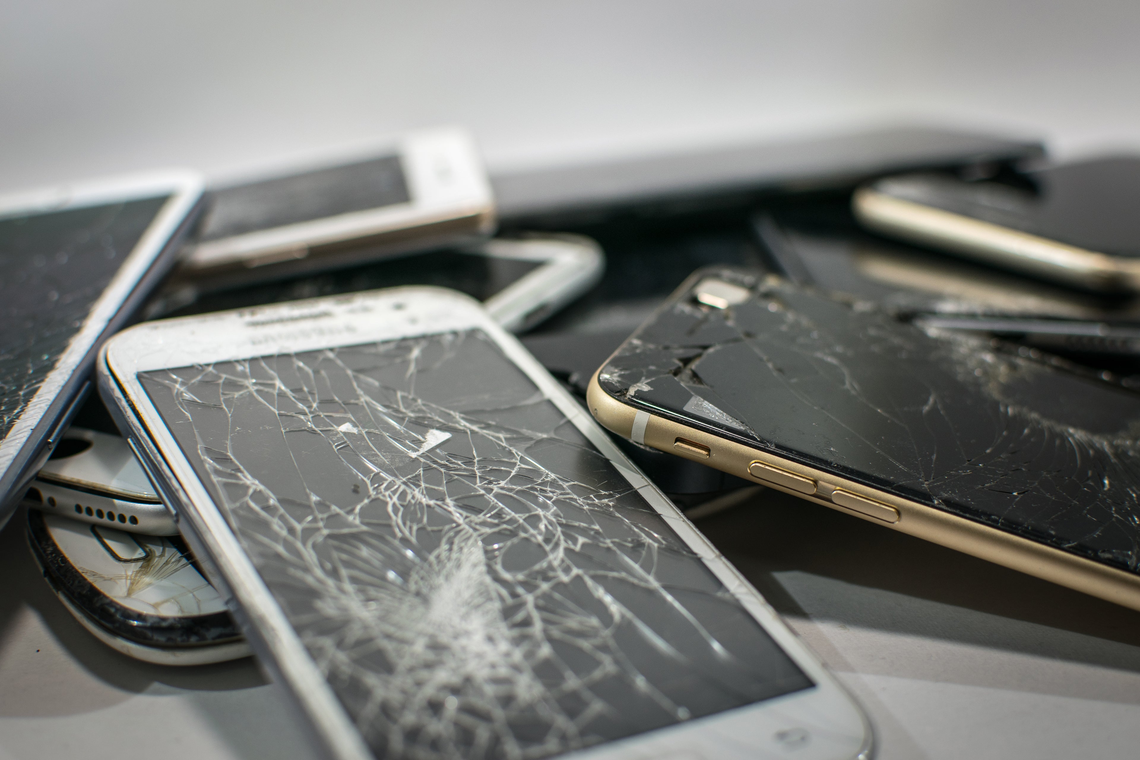 phones with cracked and broken screens lay in a pile