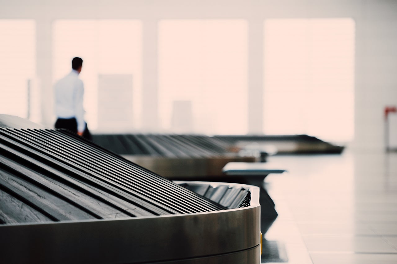 image shows a far away man looking out a window while a nearby baggage conveyor belt is empty