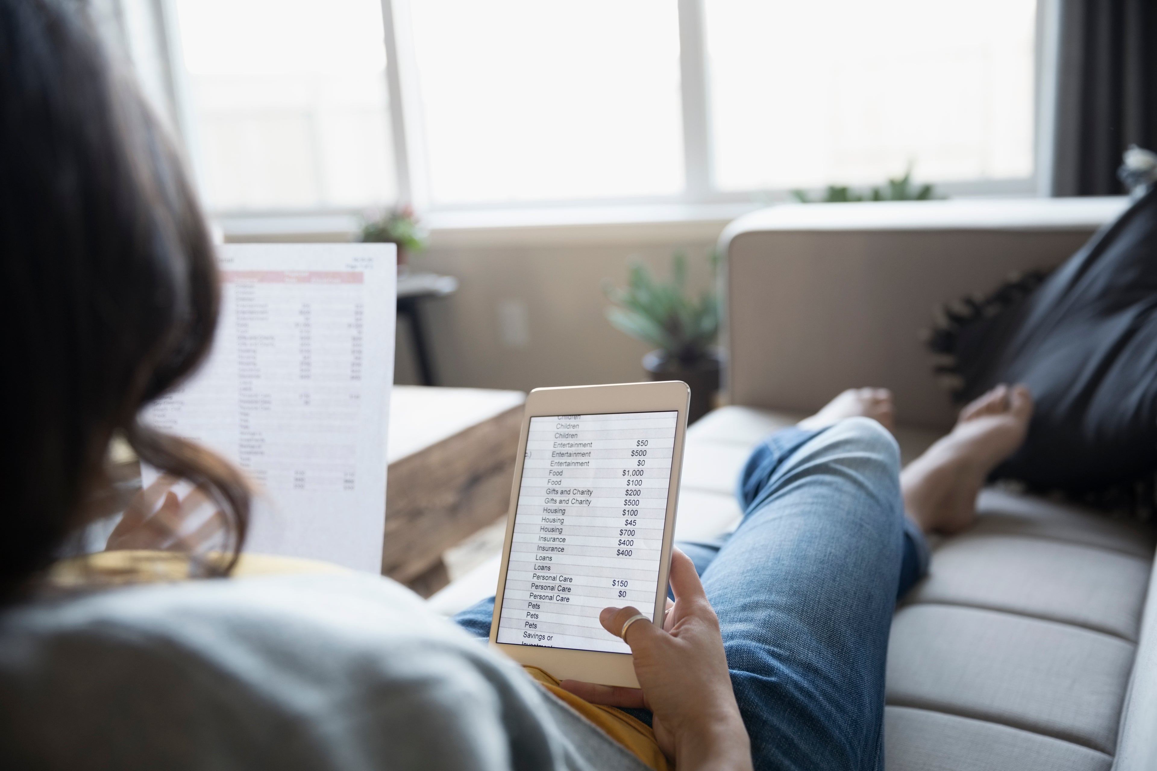 Young woman reviewing personal finances with digital tablet and paperwork on sofa