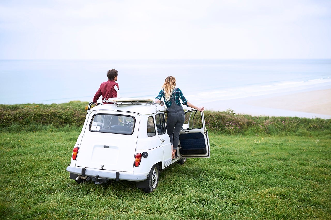 Couple in car with surf board overlooking sea on Atlantic coast.