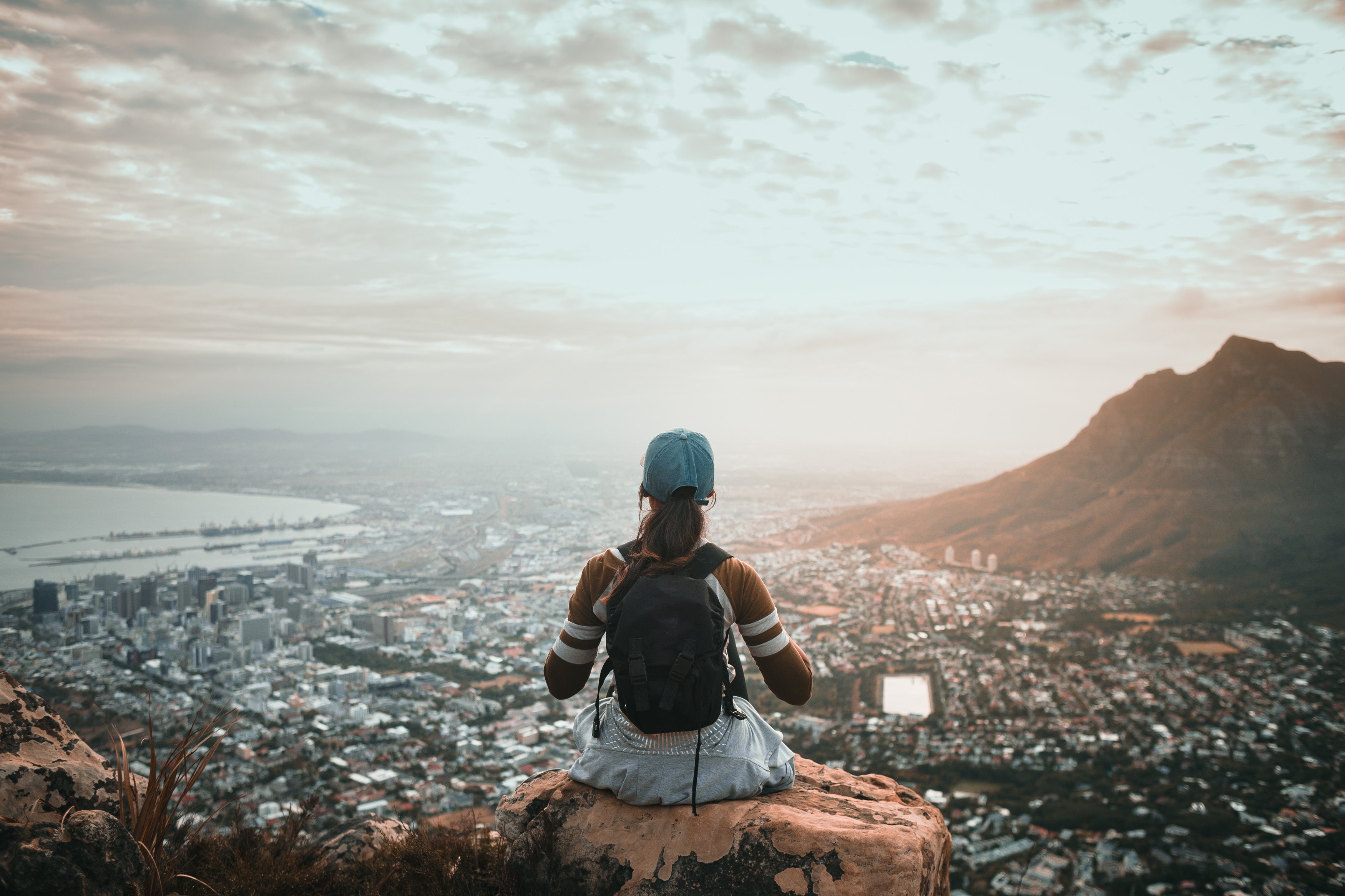 young-woman-sitting-with-backpack-overlooking-city-view-at-sunrise_t20_En80eZ