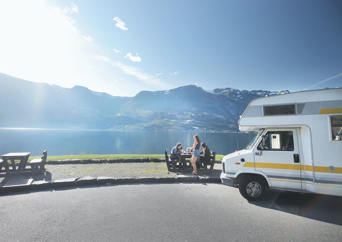 Family eating lunch out of campervan near lake and mountains