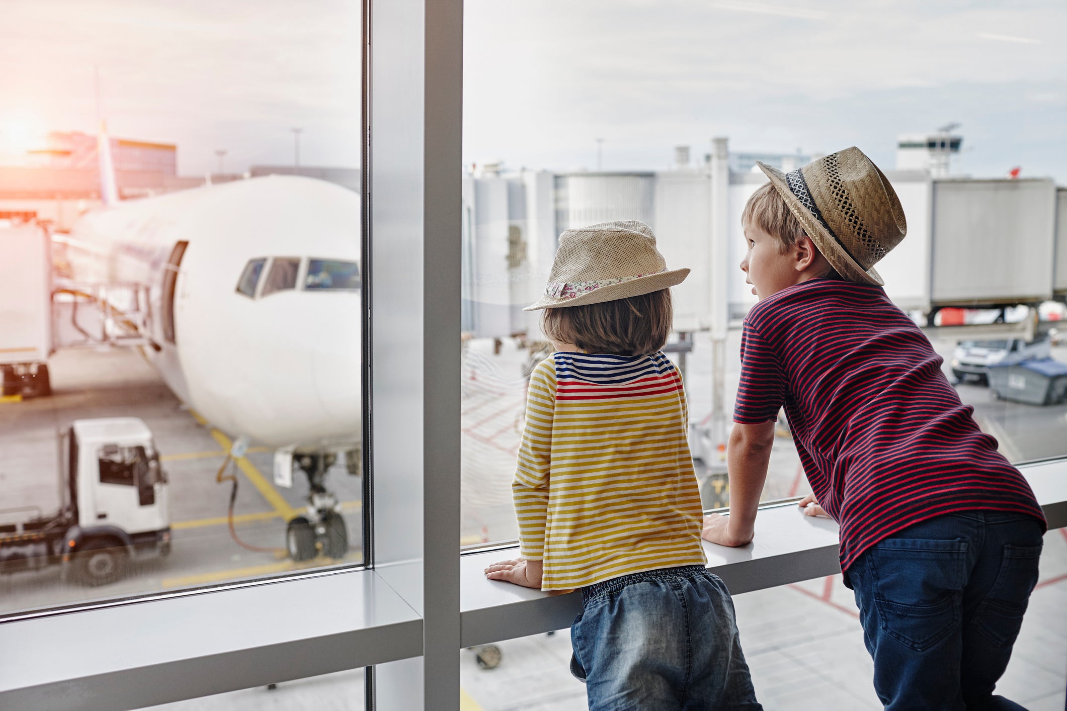 Two children wearing straw hats looking through window to airplane on the apron