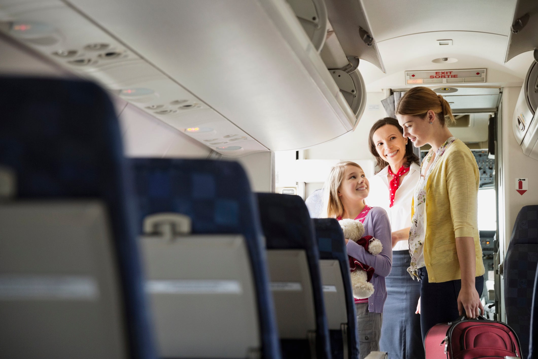 Flight attendant helping woman and daughter disembark airplane