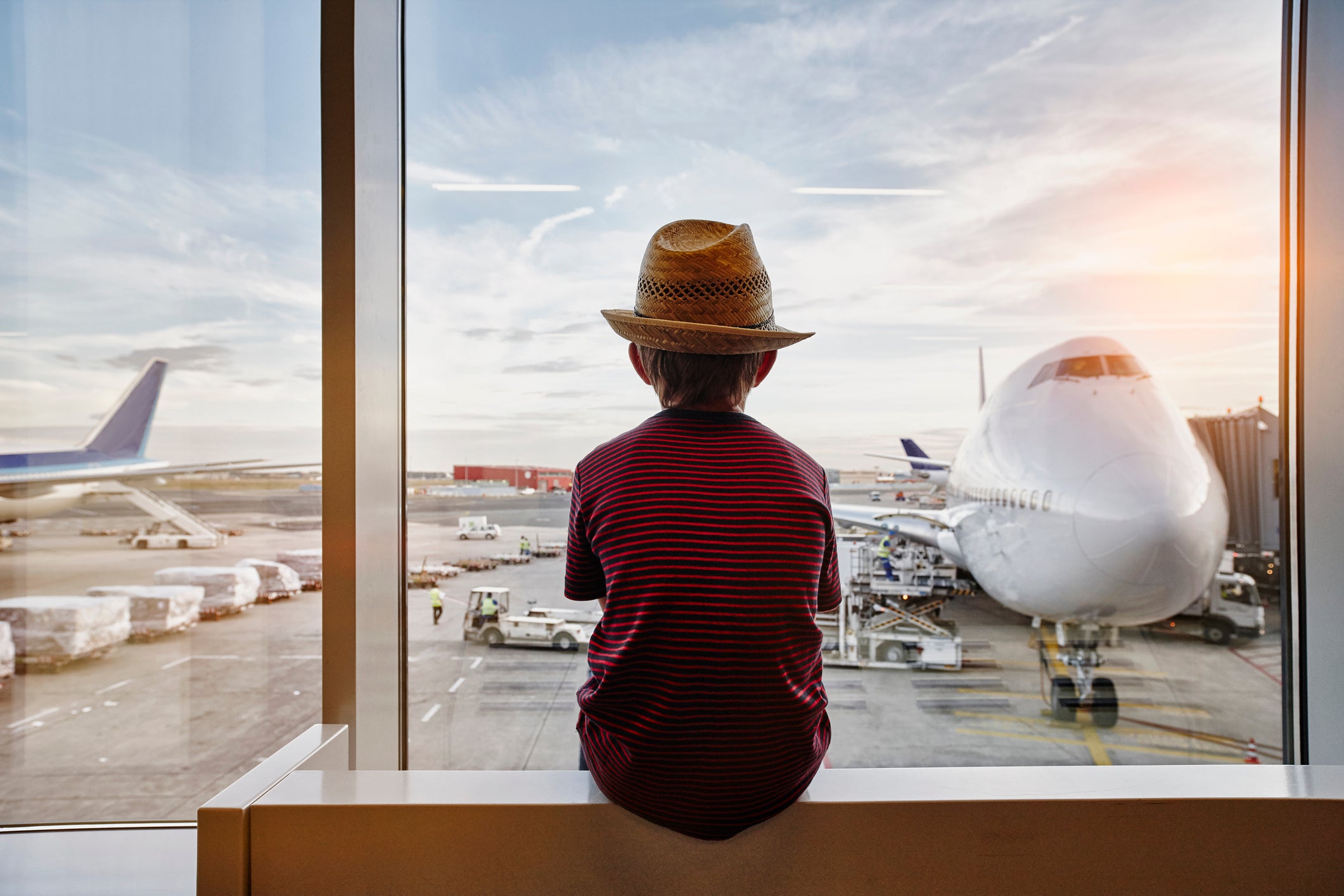 Boy wearing straw hat looking through window to airplane on the apron