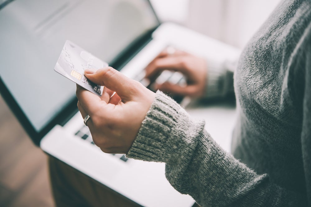 an unseen person holds a credit card while shopping online