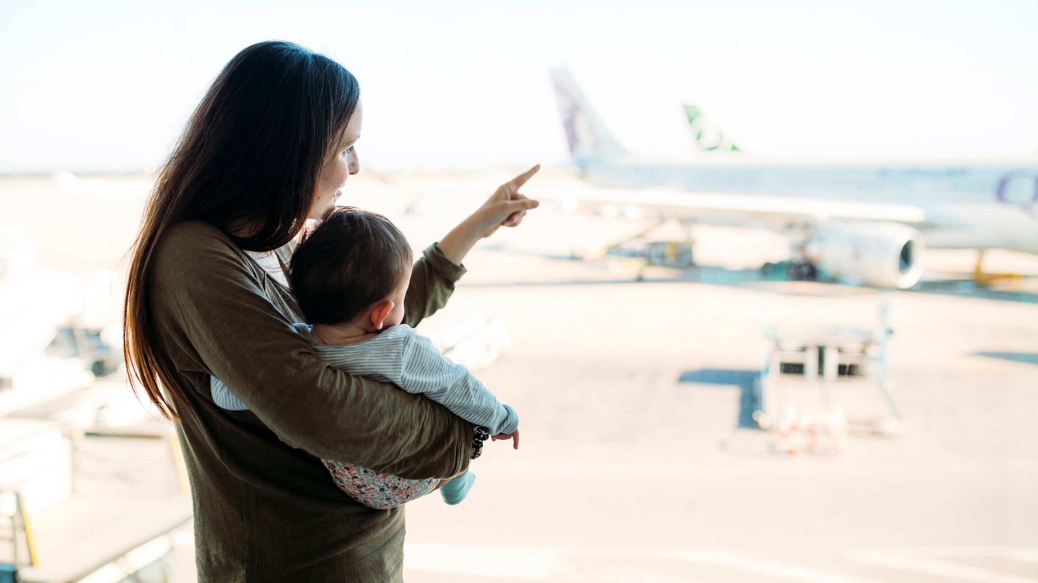 Mother holding a baby girl at the airport, pointing at the airplanes