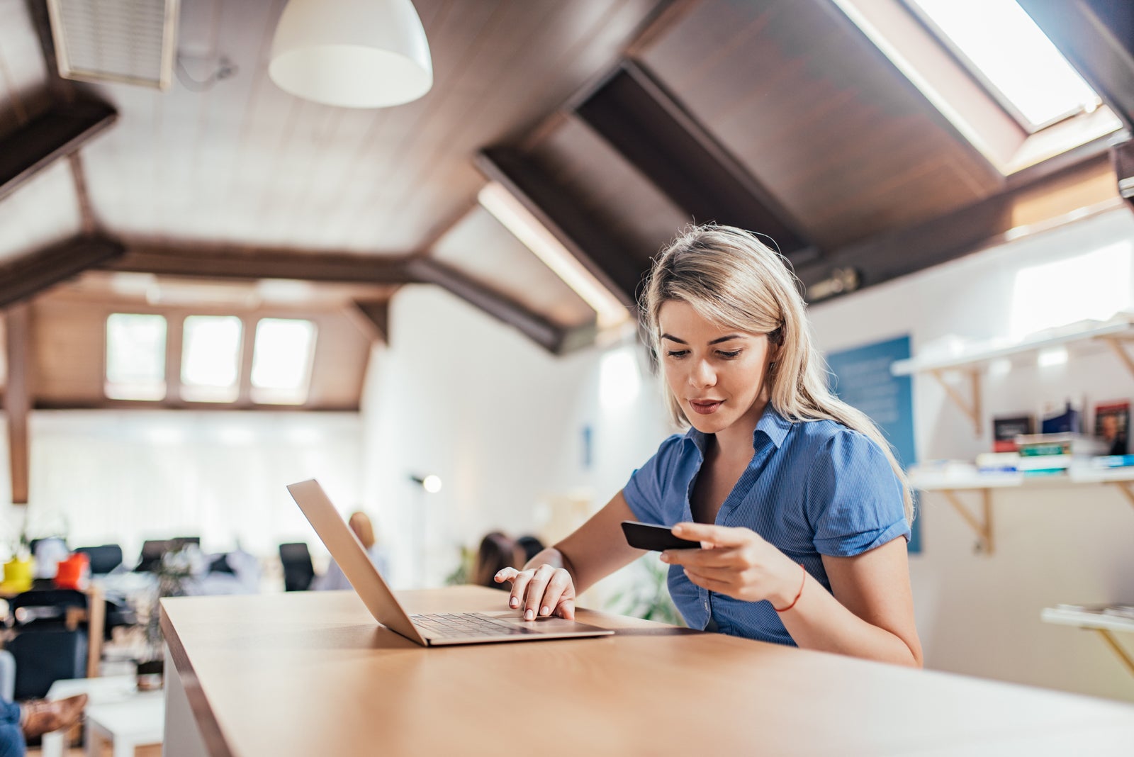 Blonde woman holding credit card and using laptop for online shopping