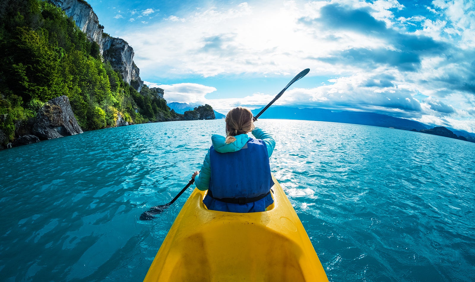 Woman paddles kayak in the lake with turquoise water