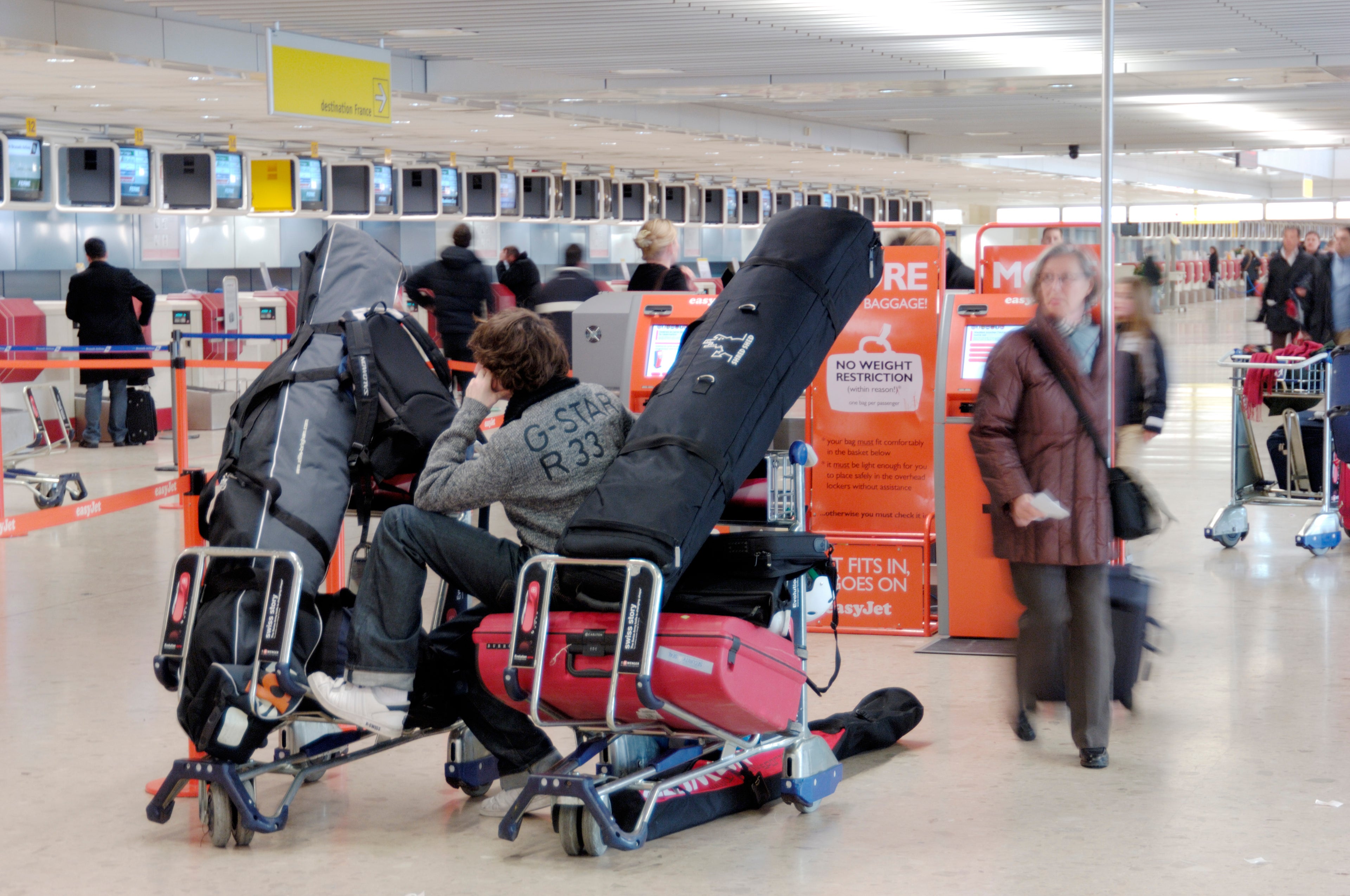 a man sitting on a baggage trolley full of luggage and skis in the easyJet check-in area