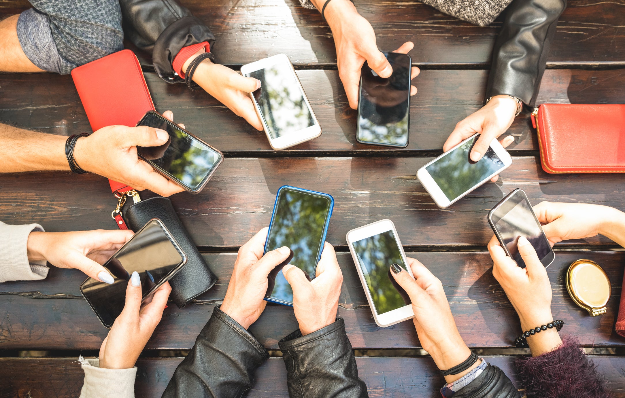 Cropped Hands Of Friends Holding Smart Phones On Table