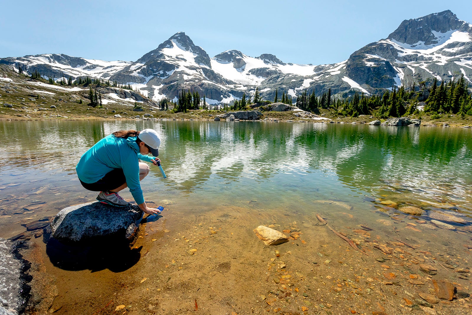 Woman filling bottle with water from lake,Pemberton, British Columbia, Canada