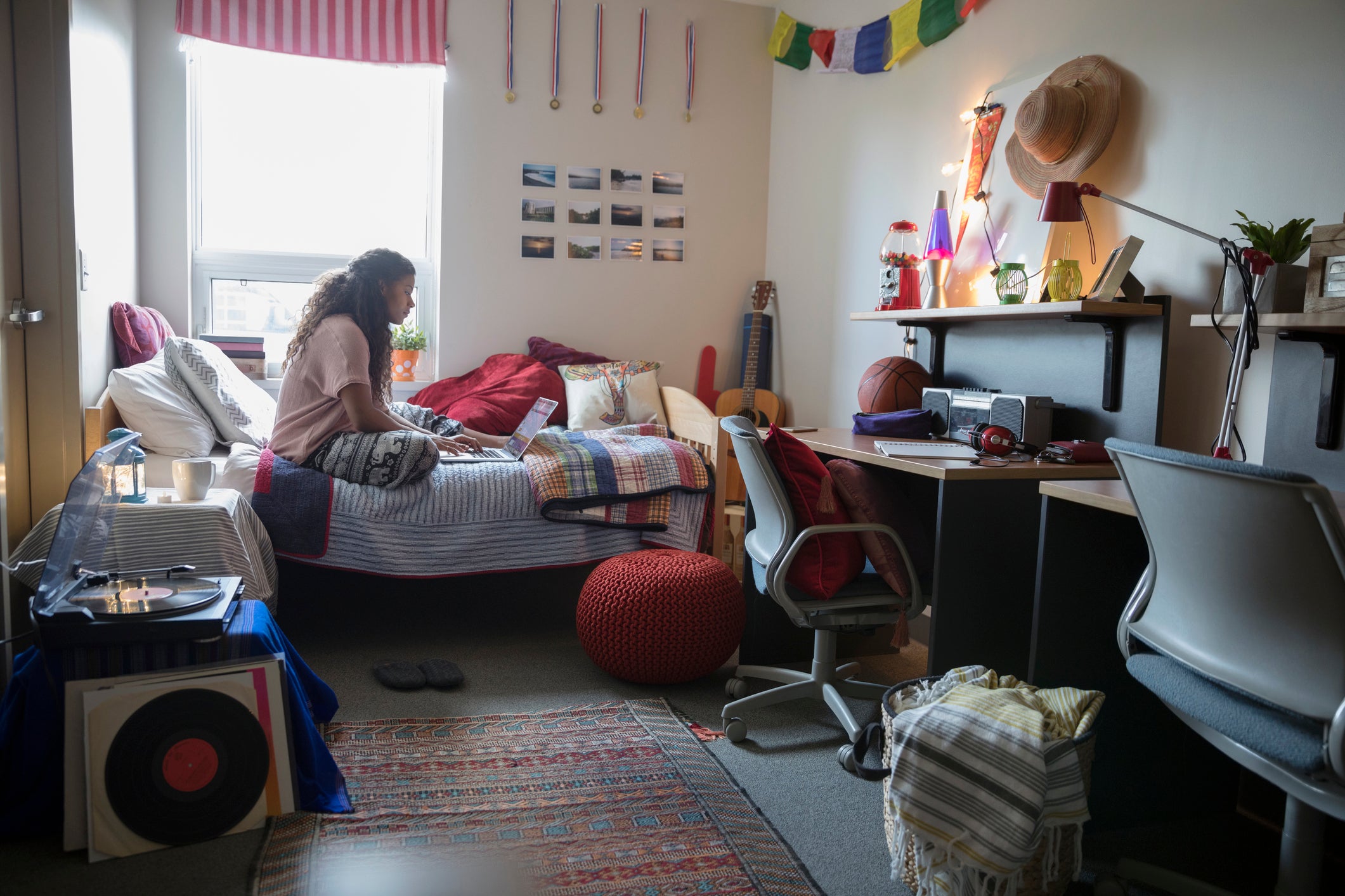 Female college student studying at laptop on bed in dorm room
