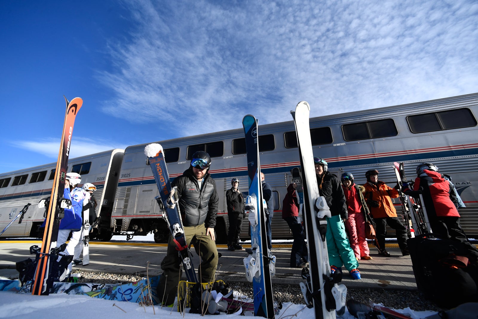 people with ski gear wait next to a train