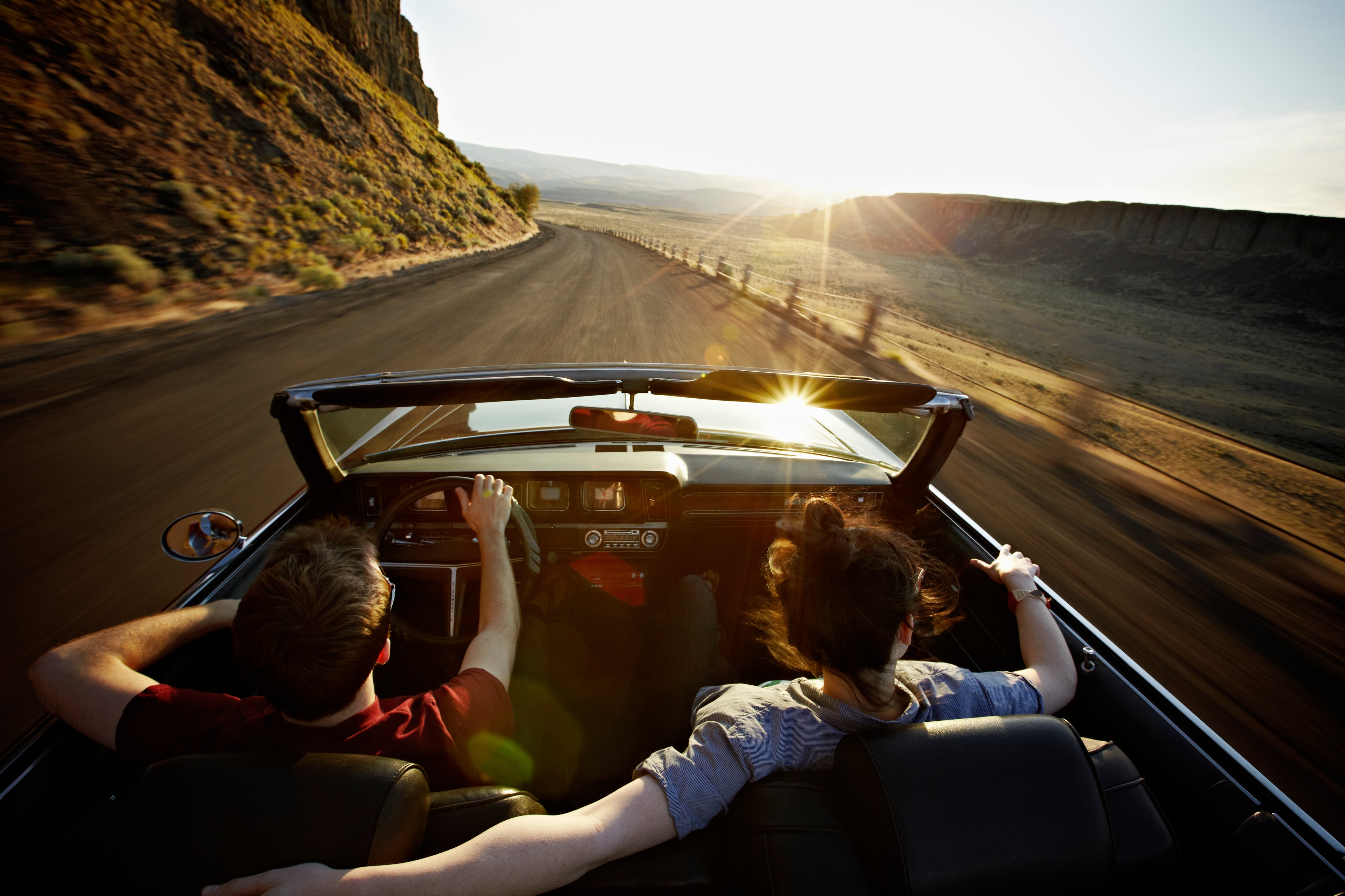 Young couple driving convertible at sunset