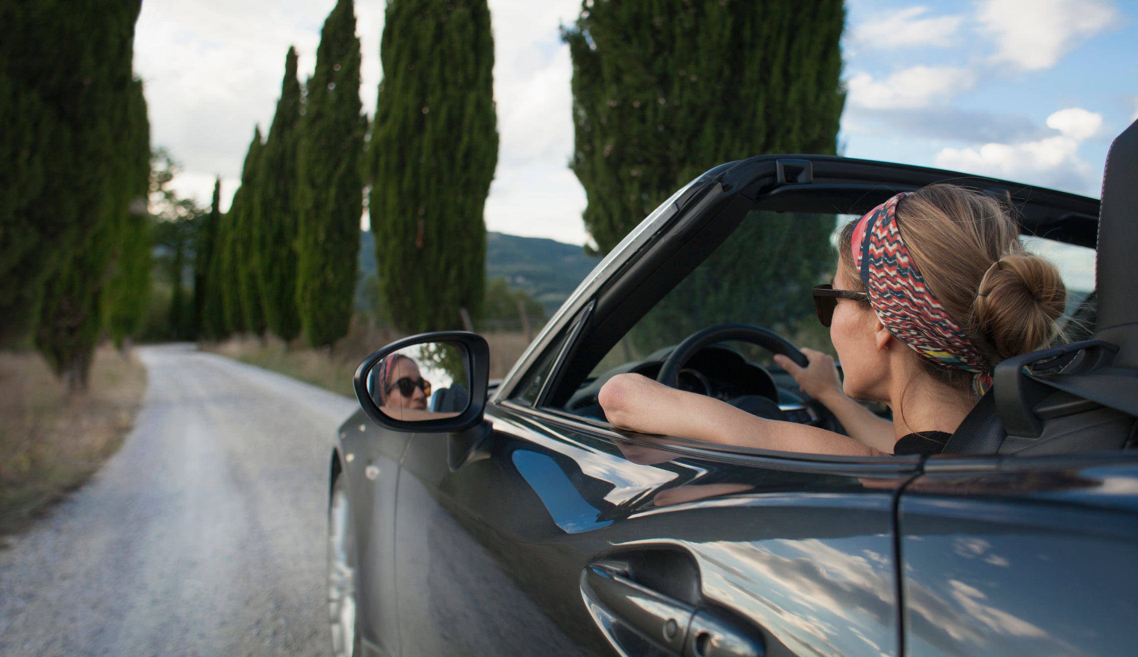 Woman driving convertible car on Tuscan country road, Italy