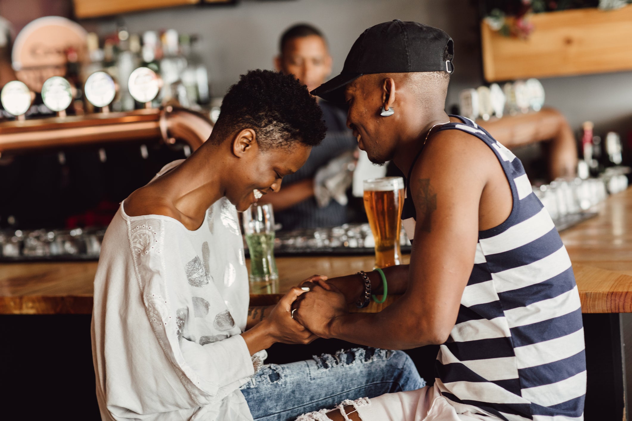 Beautiful smiling and affectionate couple holding hands whilst seated at bar drinking beer.