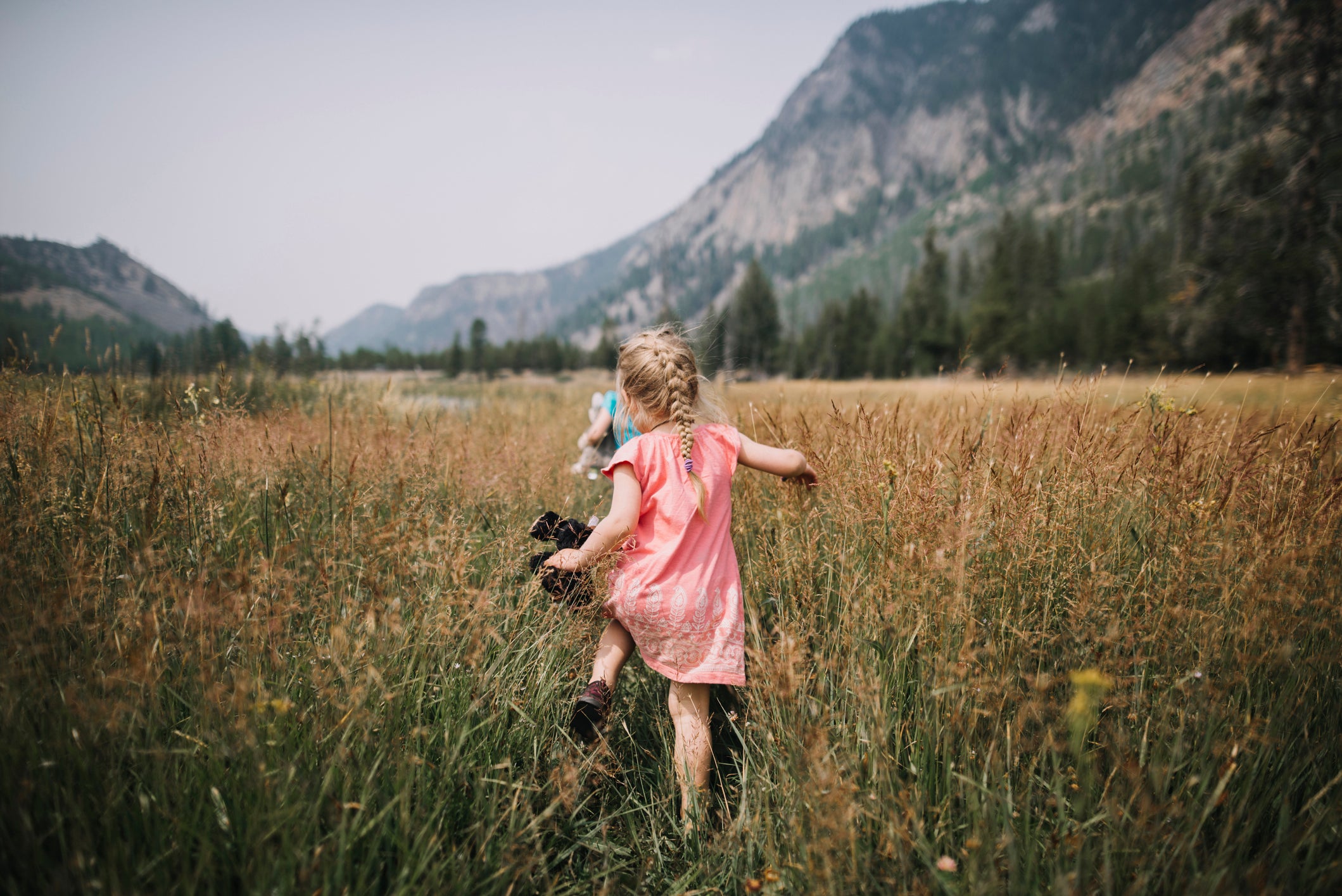 Rear view of carefree girl walking amidst grassy field against mountains at Yellowstone National Park