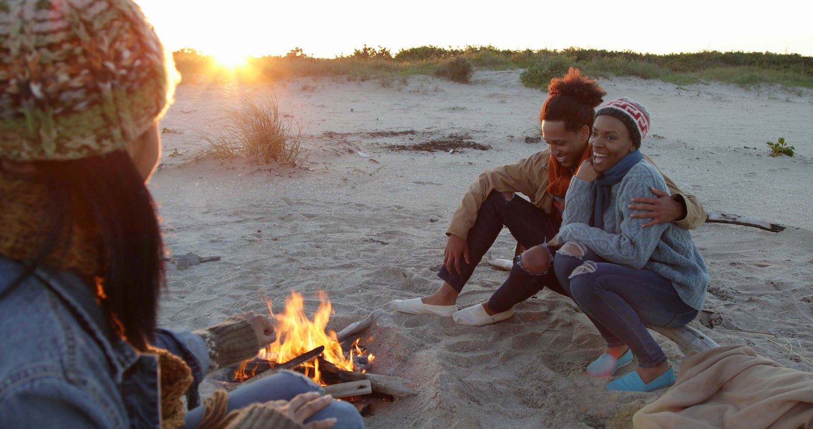 Three friends on the beach sitting beside a camp fire.