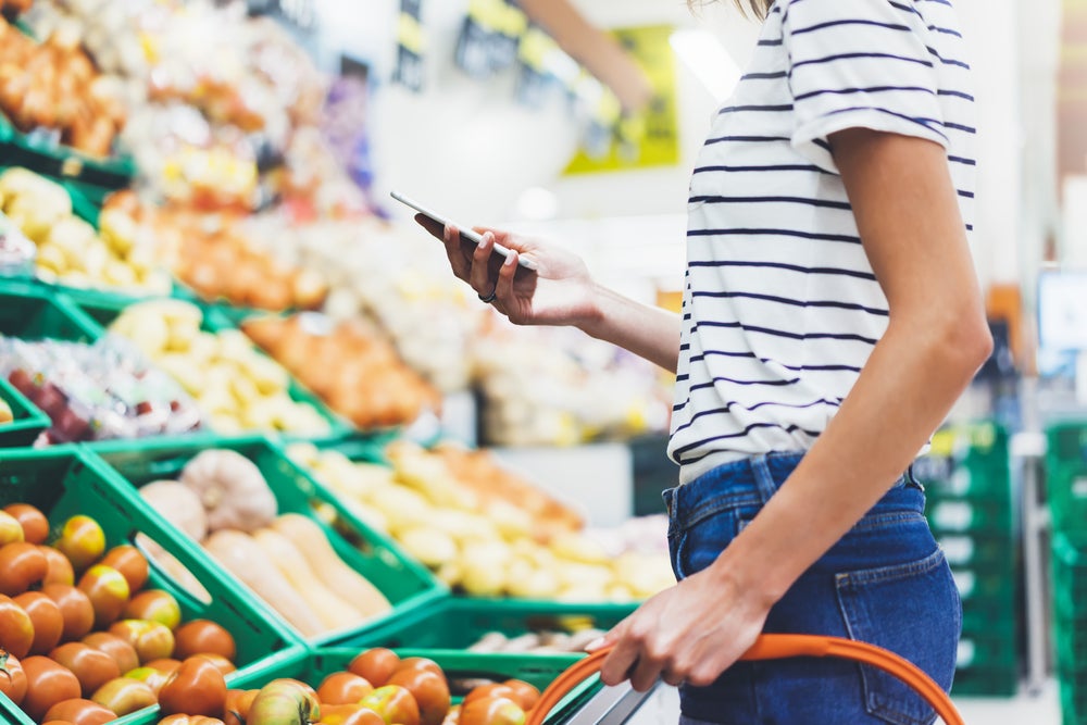 an unseen person looks at a phone near produce in a supermarket