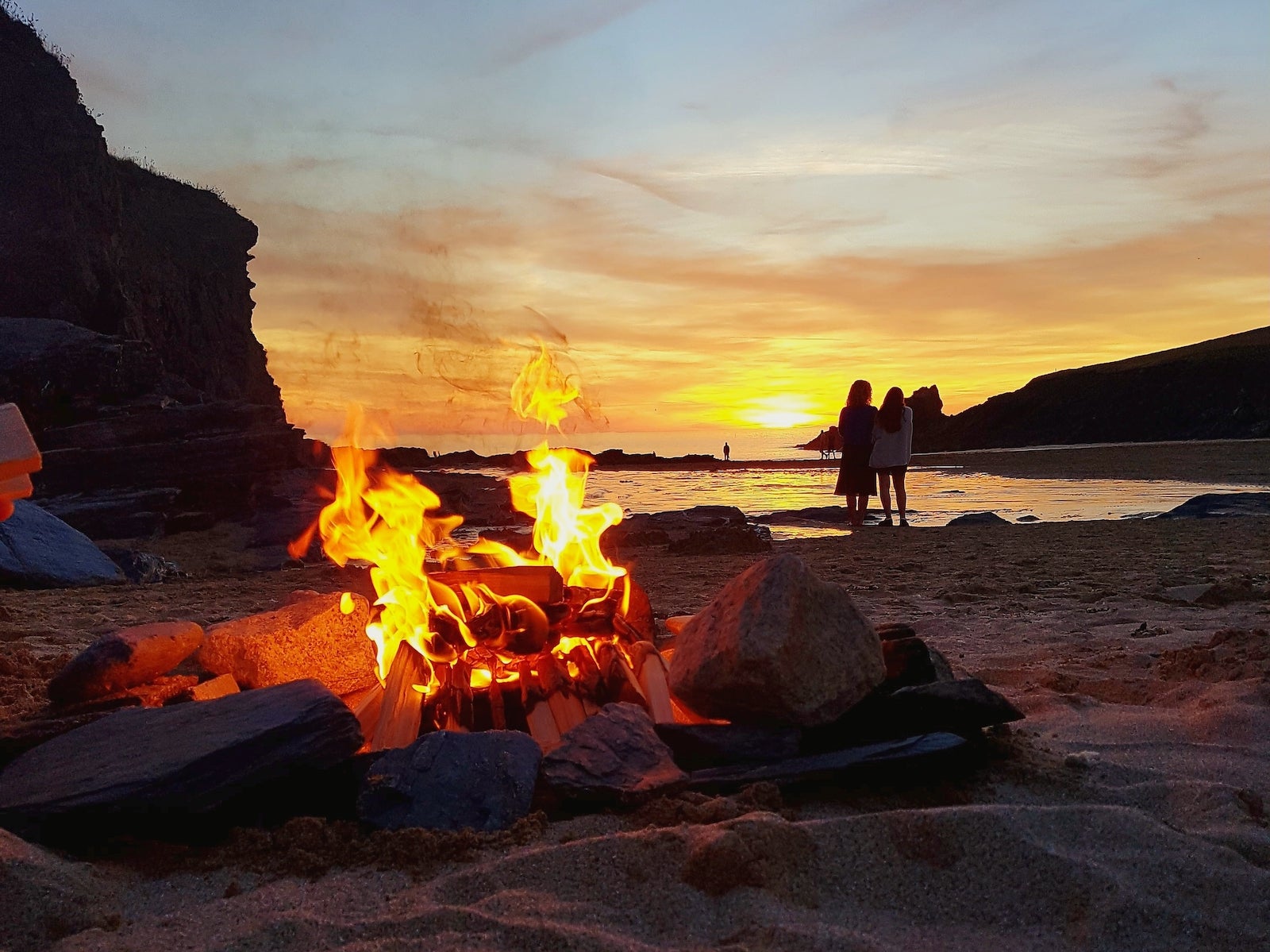 Close-Up Of Bonfire With People At Beach During Sunset