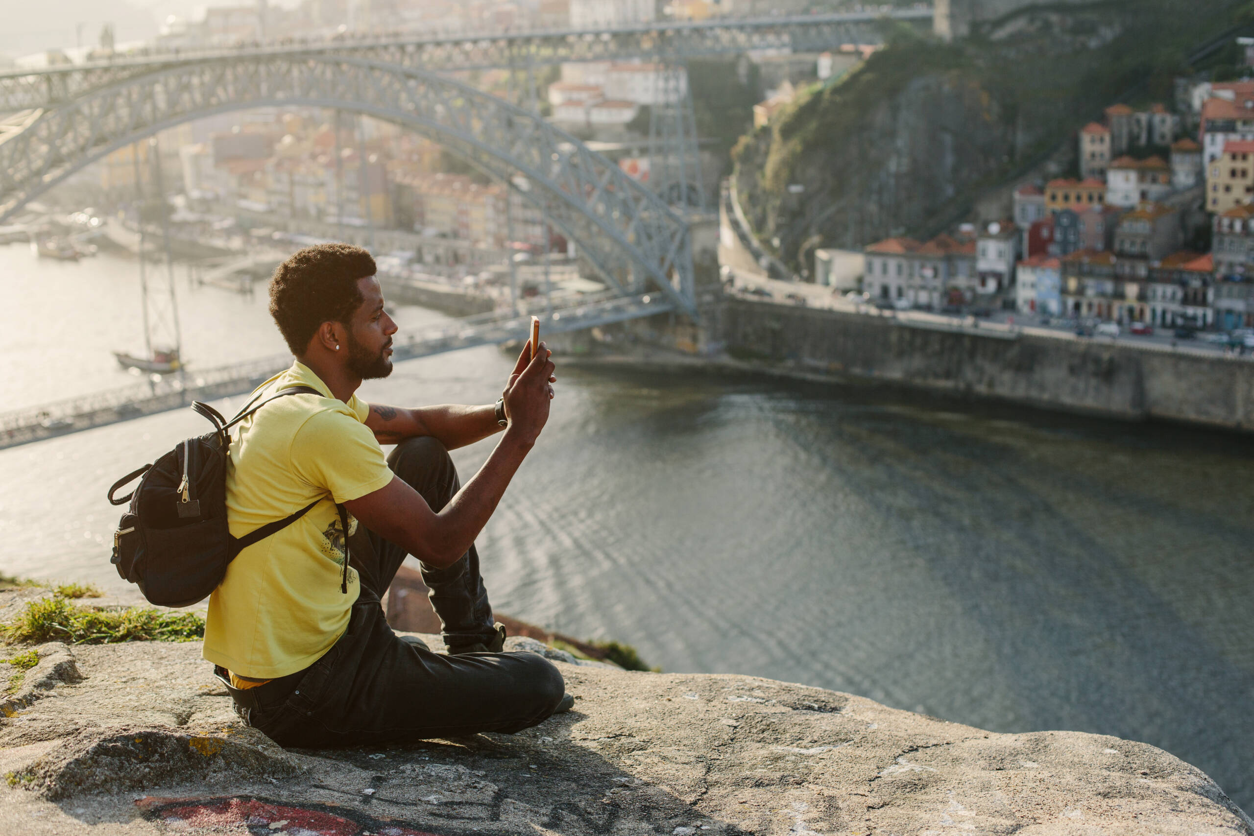 Traveler man doing photo on mobile phone. Porto, famous iron bridge and Douro rive on background