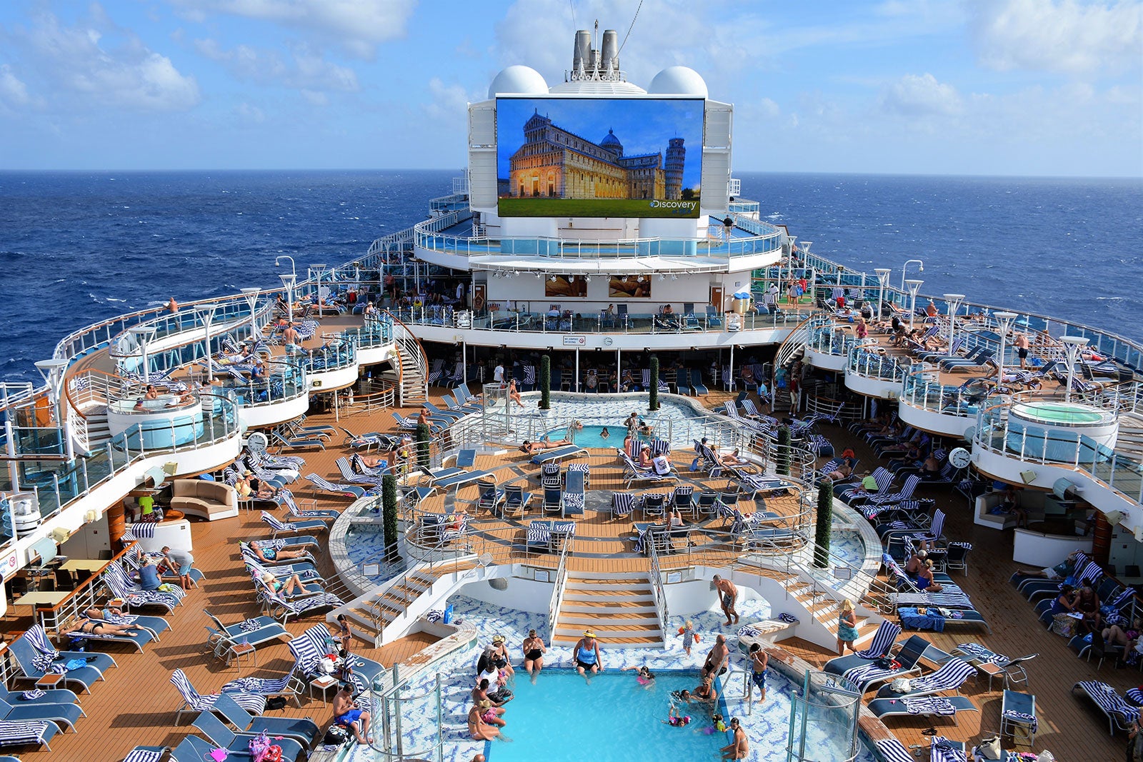 Back/ Stern and starboard side of Cruise Ship docked/ anchored/ moored in  Port with other ships. People on decks. Amazing sunset sky in background.  Stock Photo