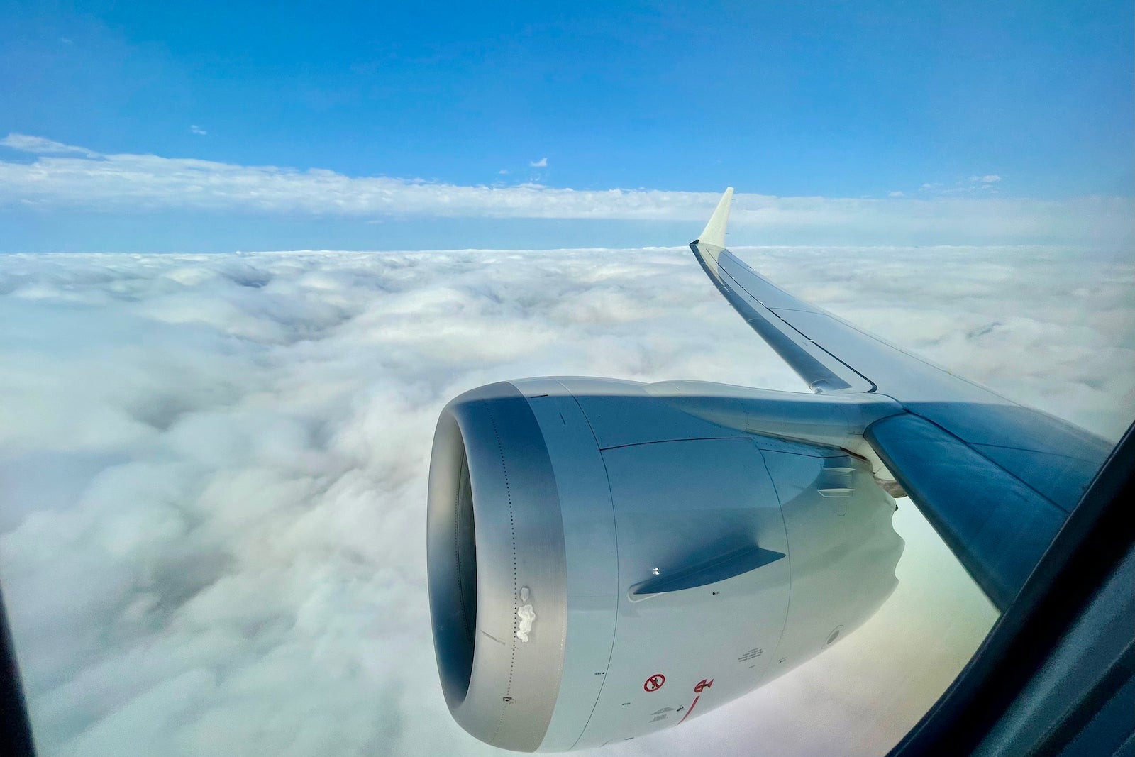 View of a plane wing and engine above a cloudy blue sky mid-flight
