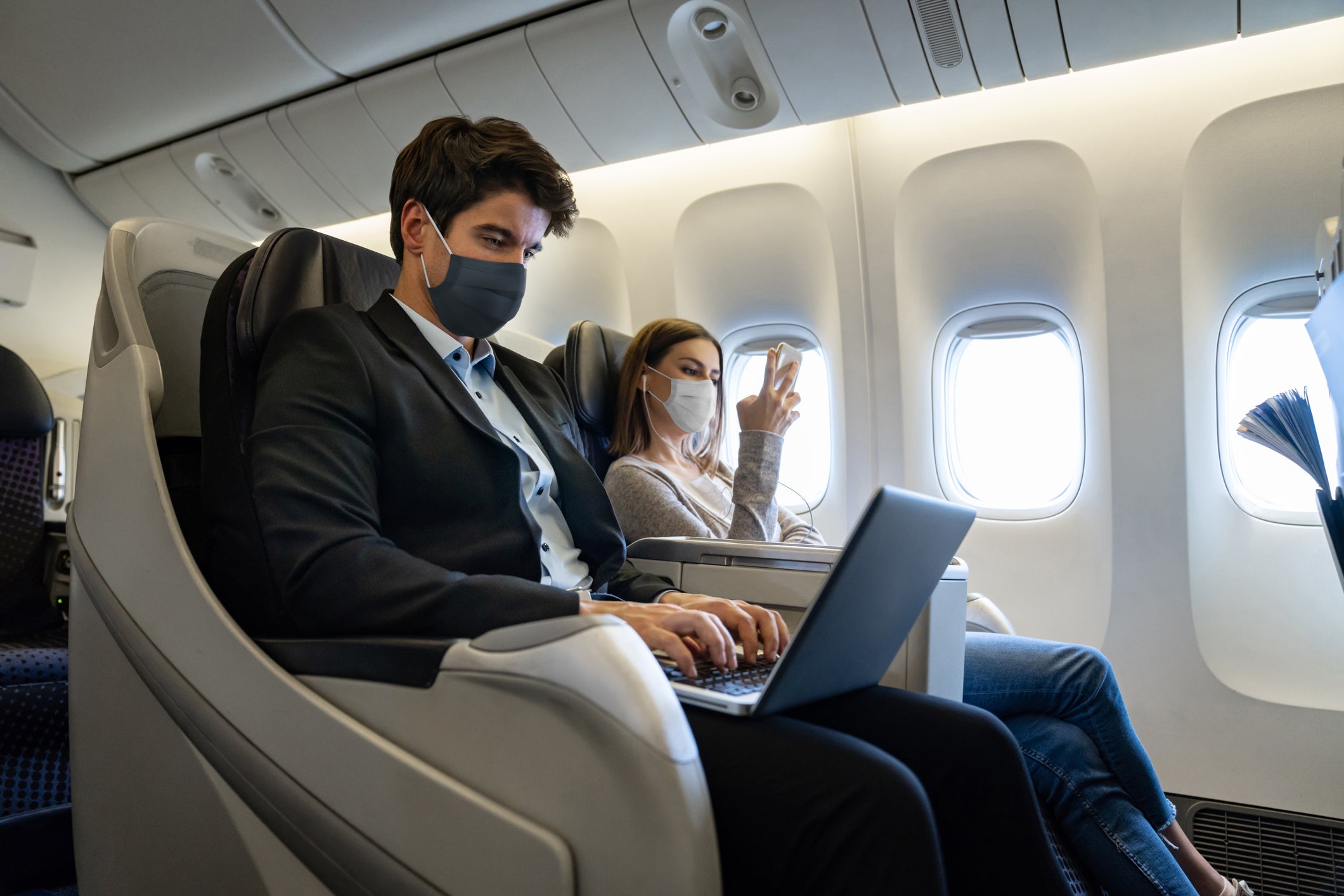 People traveling by air in business class and wearing facemasks on the plane - COVID-19 pandemic lifestyle concepts