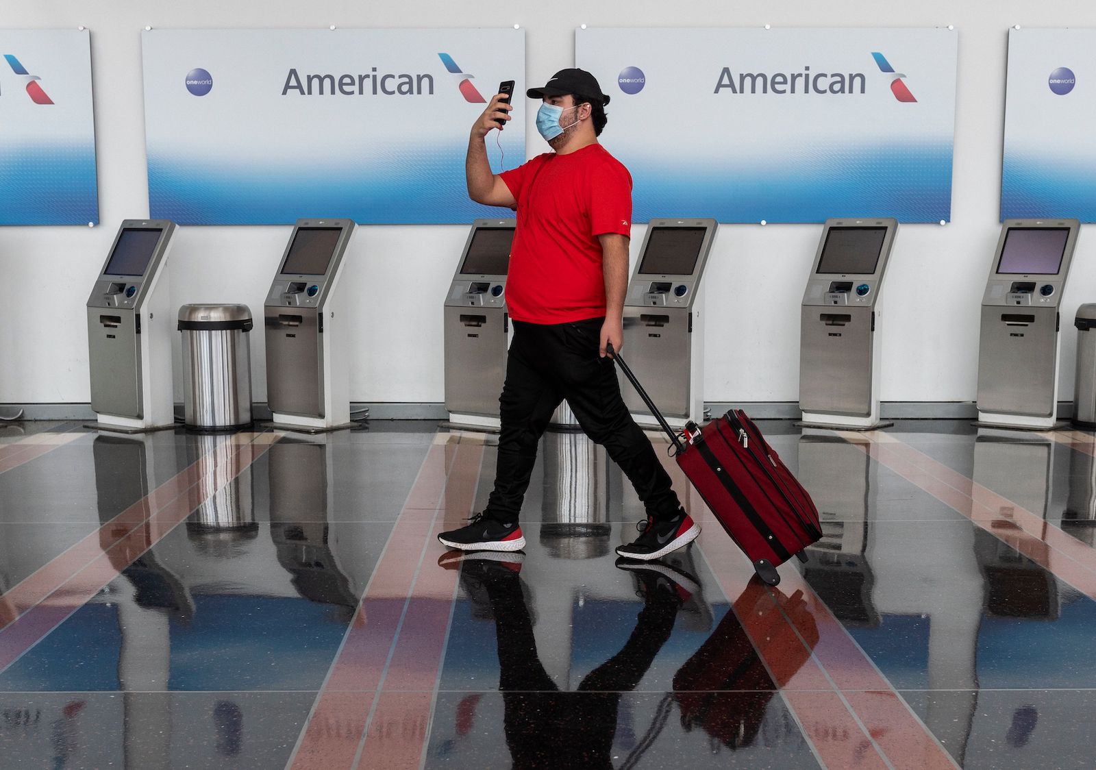 Man wearing a mask walking with a suitcase by an American Airlines sign