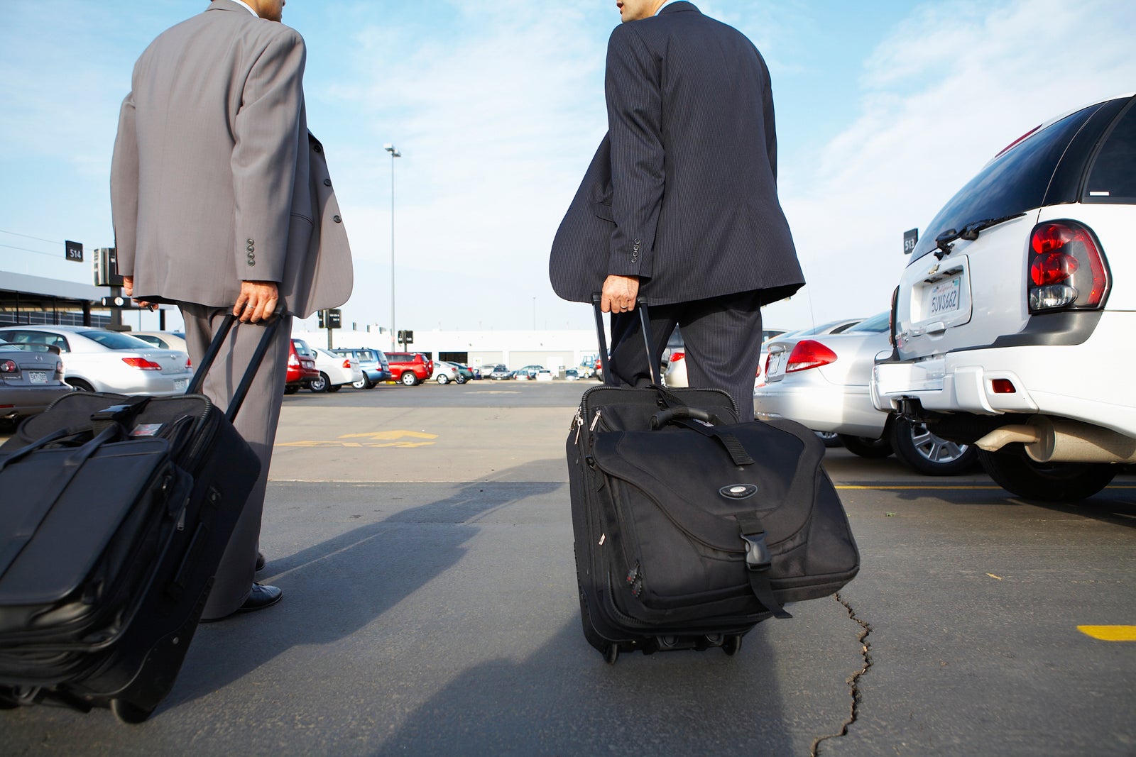 Two business men pulling suitcases through car rental lot, rear view