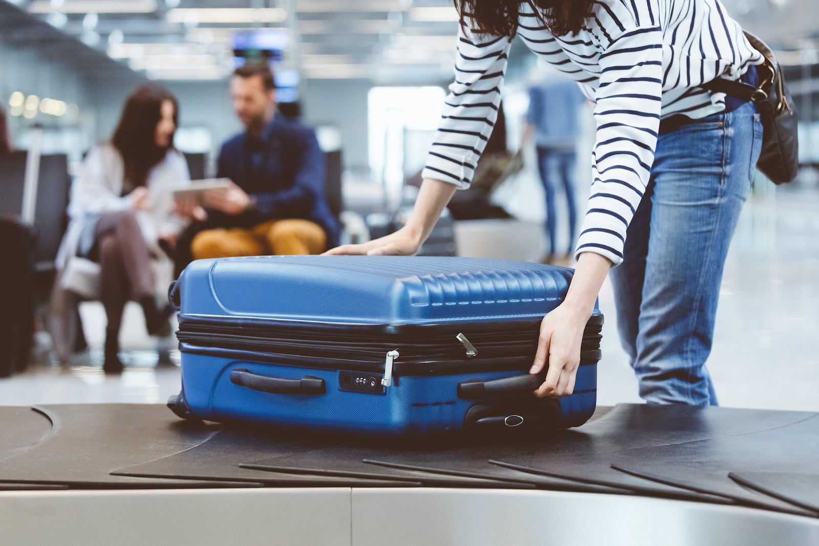 an unidentified person reaches for a blue suitcase on a conveyor belt