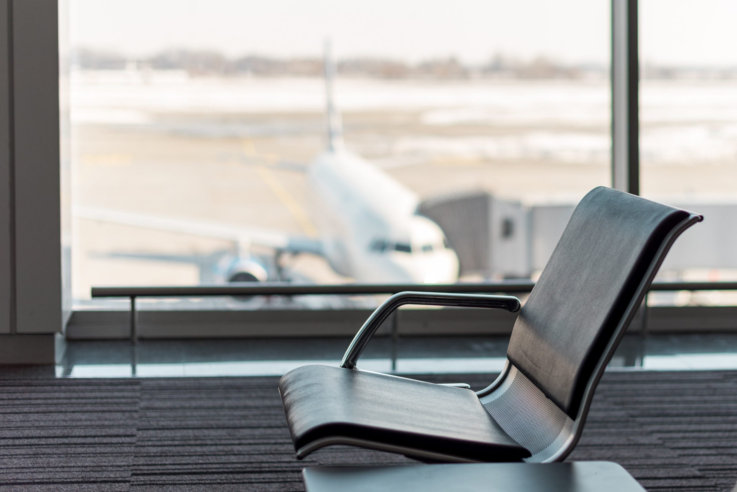 The waiting hall in airport terminal, focus on the seats and blurred aircraft behind the window. Vacation concept, beautiful summer travel background