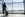 Young man is standing near window at the airport and watching plane before departure. He is standing and carrying luggage. Focus on his back