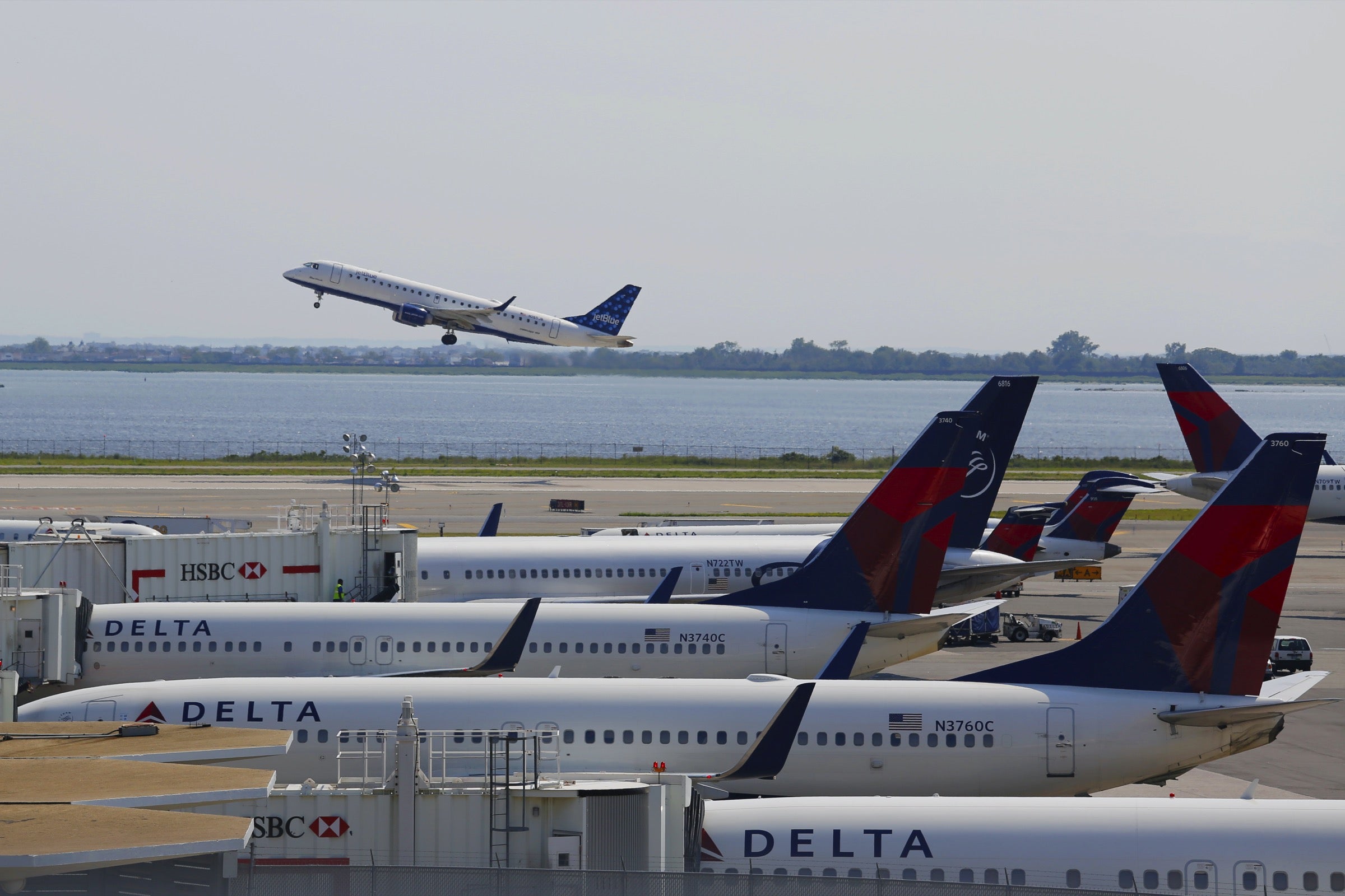 JetBlue plane taking off next to parked Delta planes at JFK