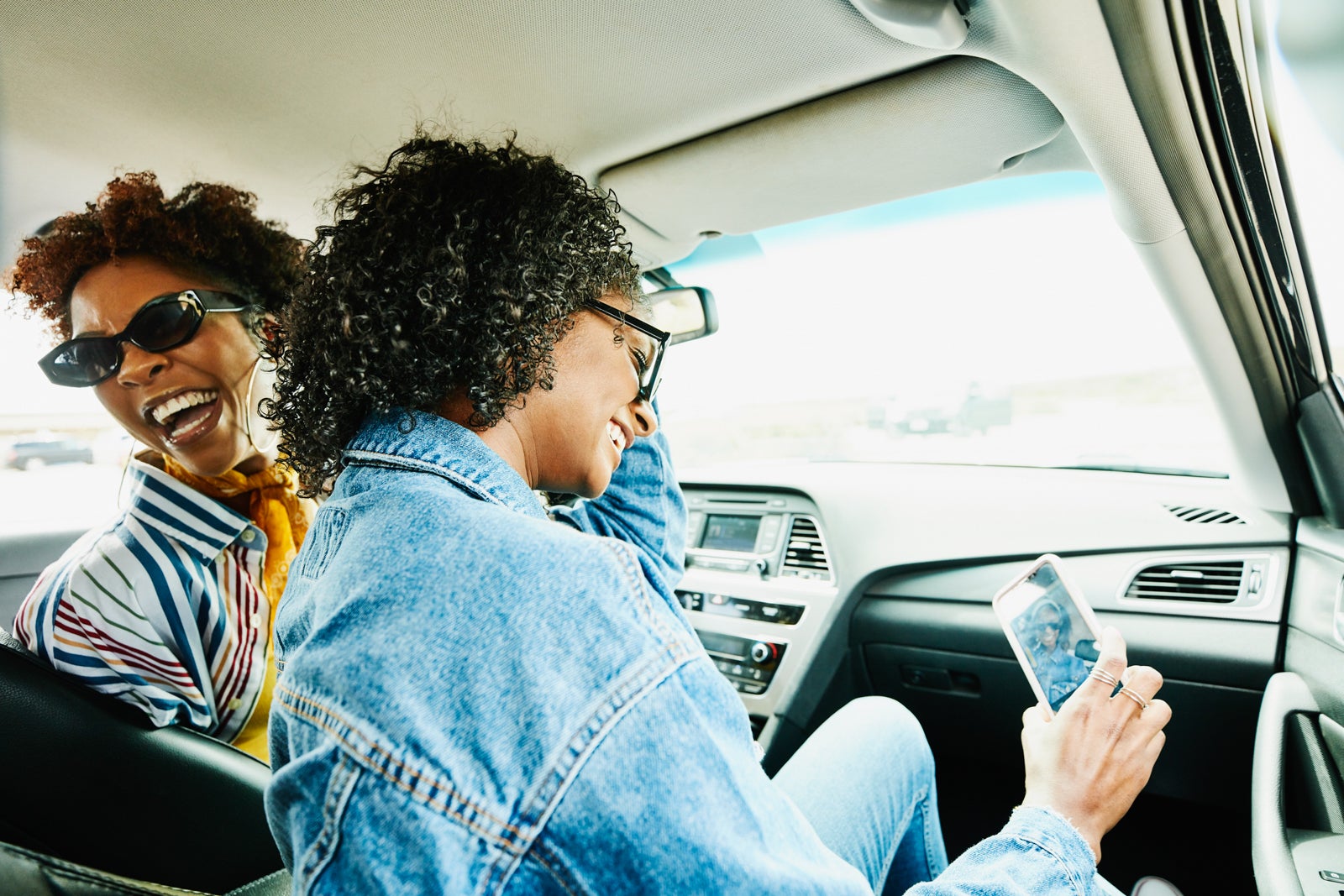 Smiling woman taking selfie with smart phone while sitting in passenger seat of car during road trip with friends