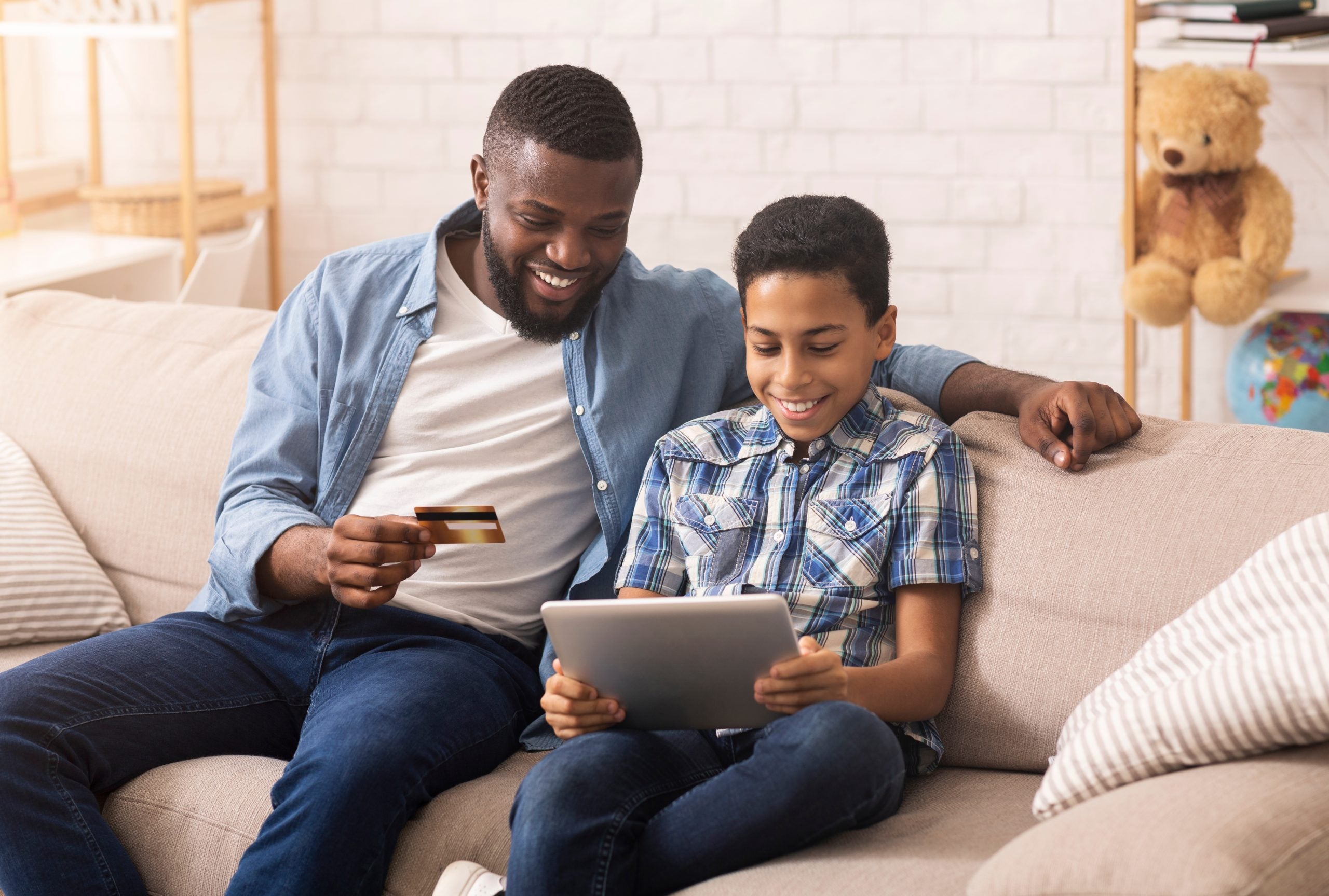 a father teaches a son about credit cards while they use a tablet