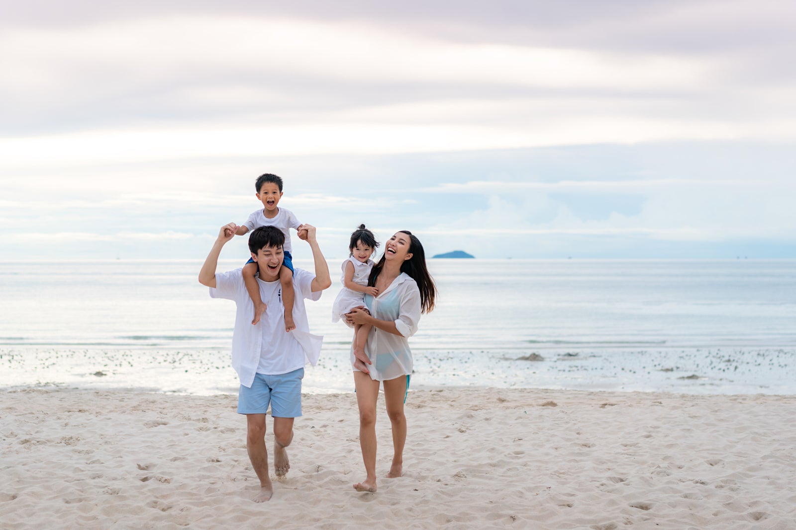 Happy Asian family holidays during joyful father, mother, son and daughter walking together along summer sunset sea. Happy family travel on beach in holiday, Summer and vacation.