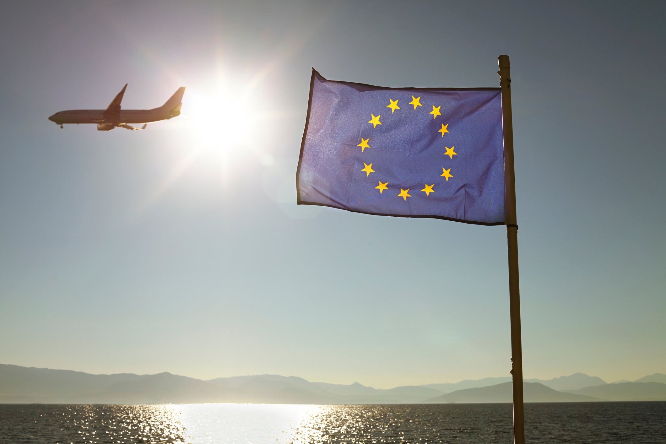 European Union Flag Against Sun &amp; Sea With Plane
