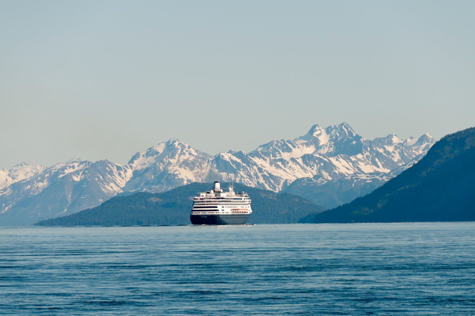 cruise ship sails in the water with snow-capped mountains in the background
