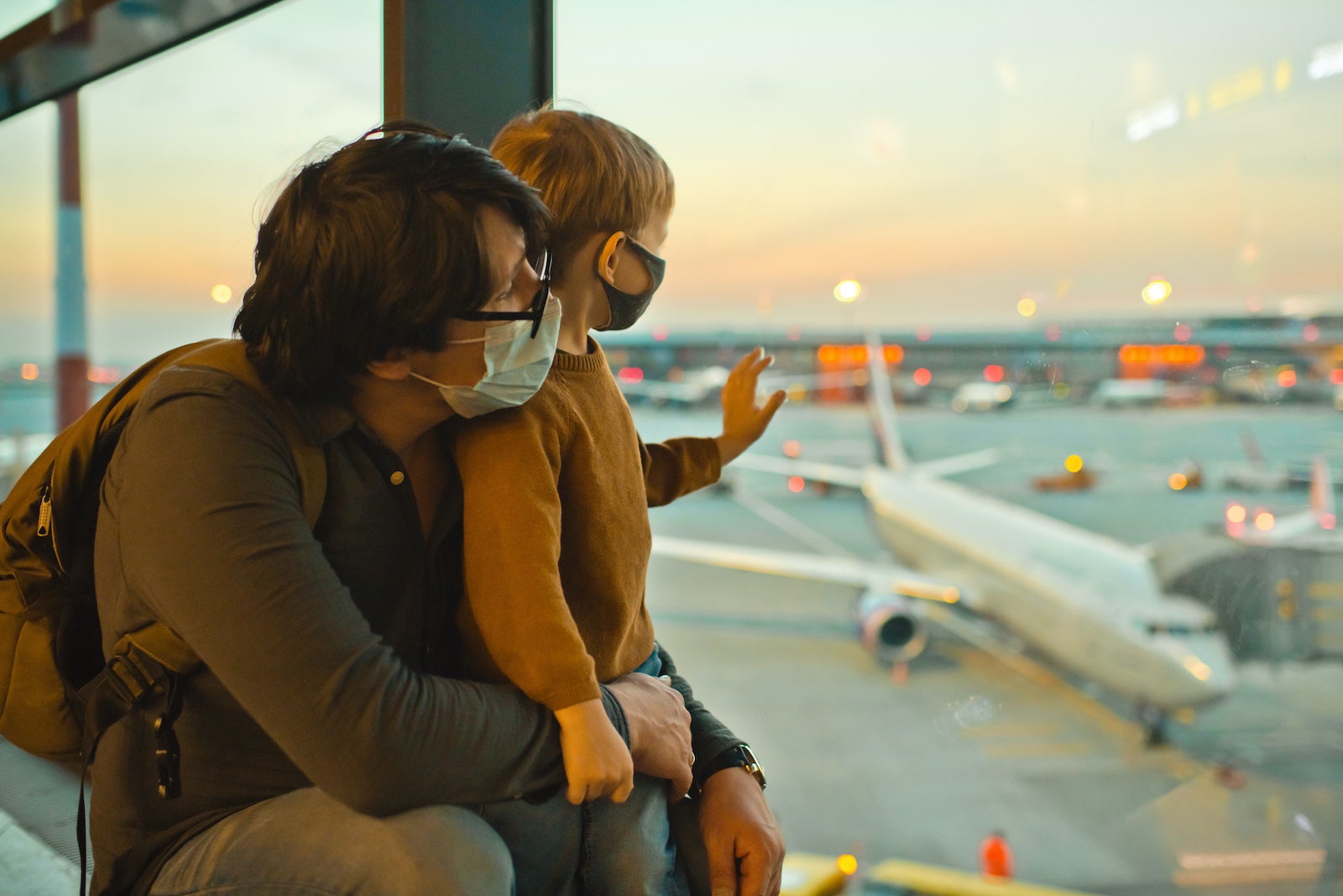 Dad and son wearing masks and looking out of an airport window.