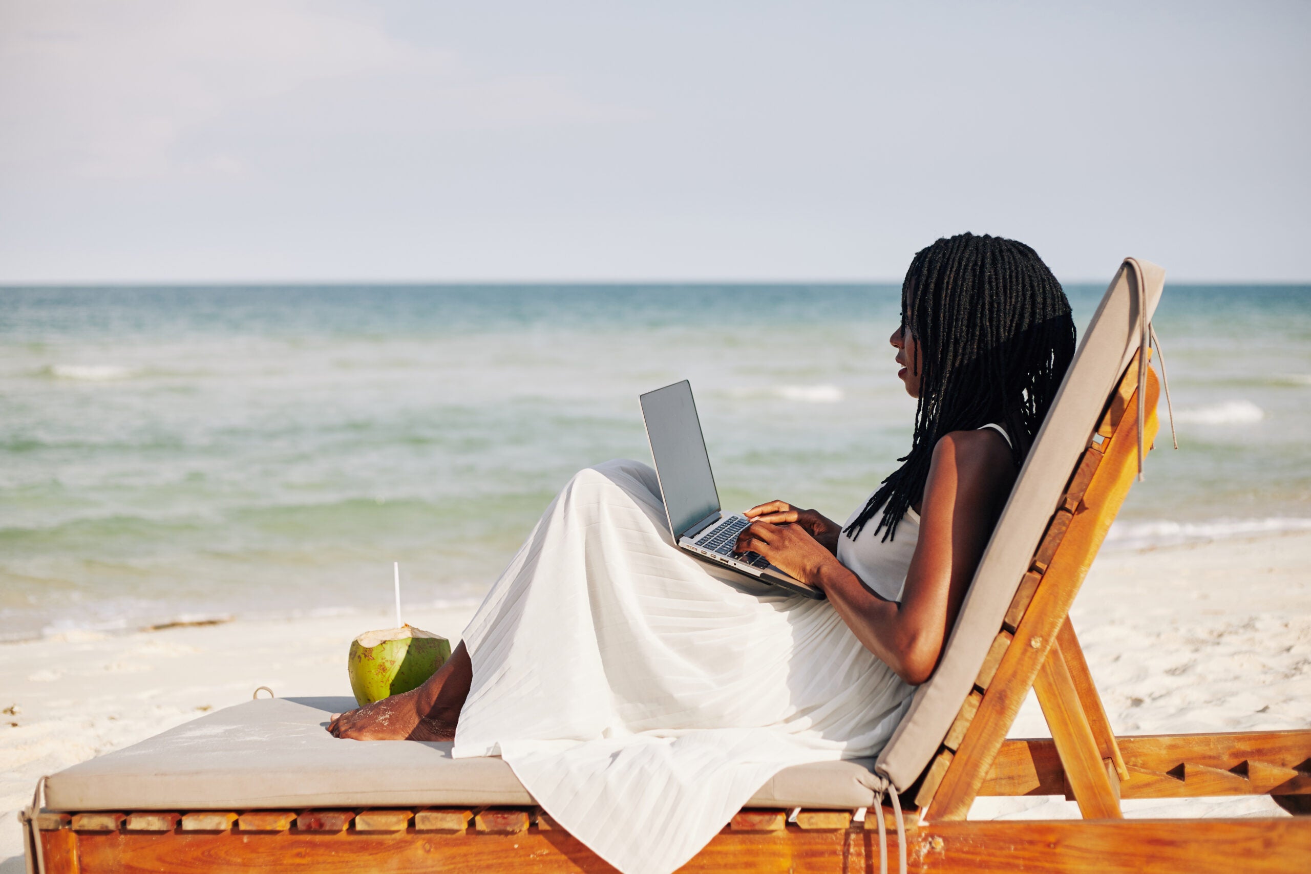 Woman sits on a beach chair on computer.