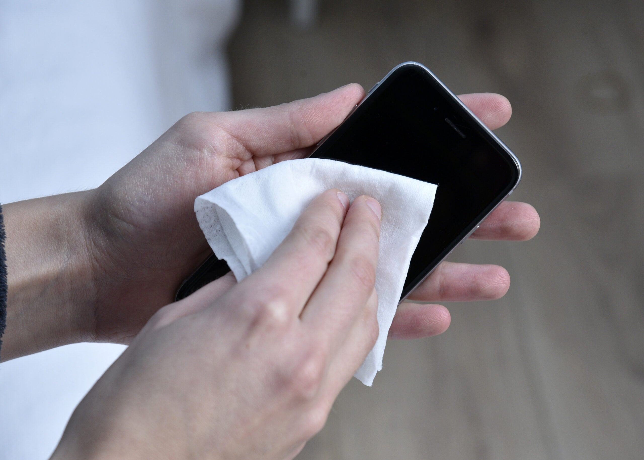 one hand holds a smart phone while another wipes the phone's face with a cloth