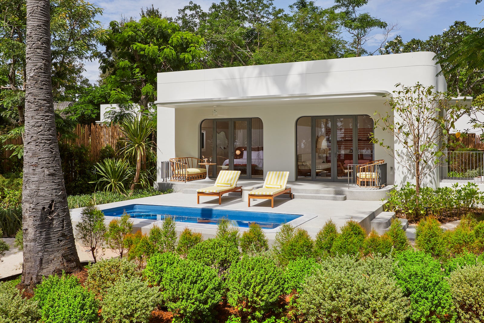 white building with yellow and white chairs, plunge pool, lush greenery