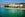 shot of large white hotel with red roof sitting on beach with blue-green water