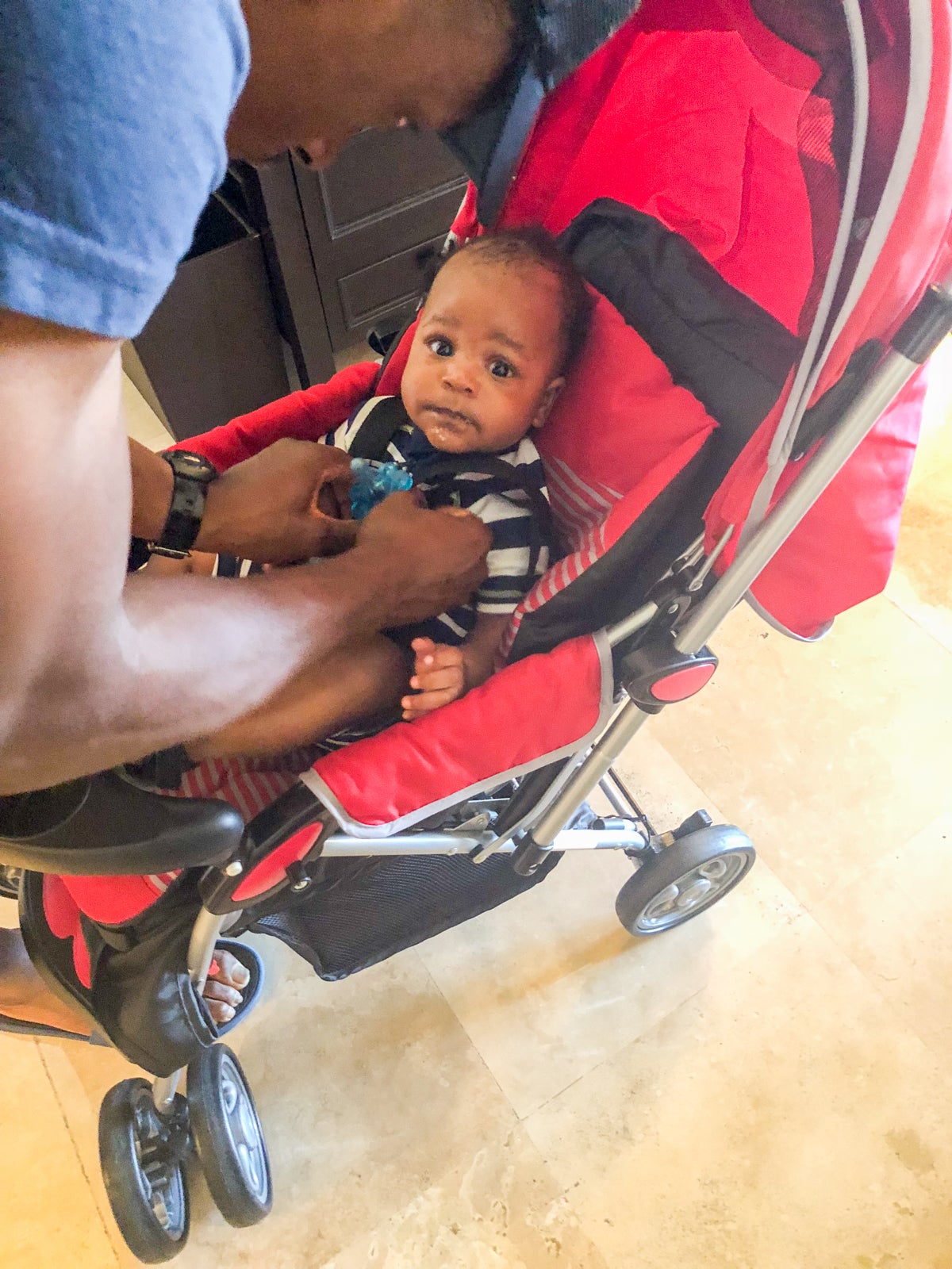 Baby being strapped into a red stroller.